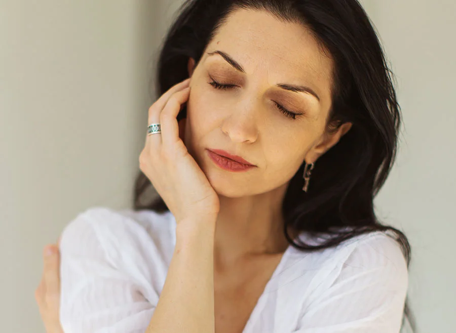 A woman with closed eyes, resting her hand against her cheek, creating a soft, peaceful expression in warm, natural light - Mesotherapy in Frisco, TX