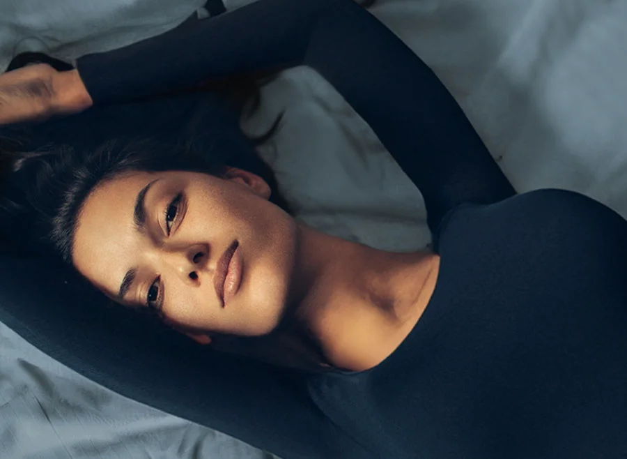 A woman in a black long-sleeved top lying on her back with her arms stretched above her head - Pigmentation and Melasma Treatment in Frisco, TX