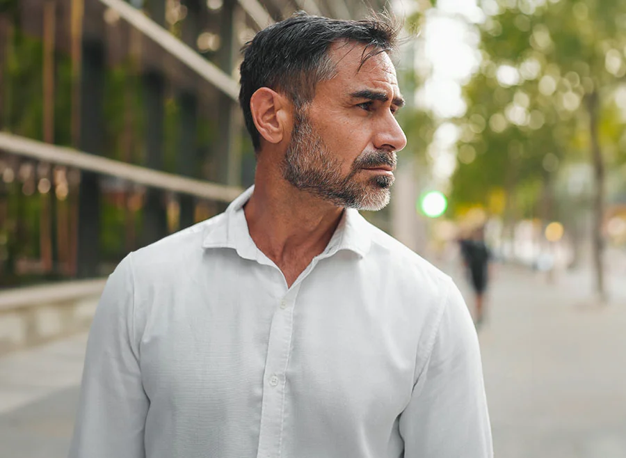 bearded middle-aged man in a white shirt standing outside in a modern cityscape, gazing thoughtfully into the distance - PRP Hair Restoration in Frisco, TX