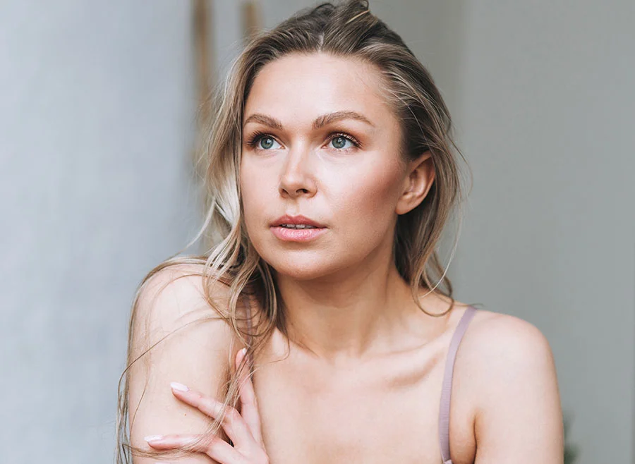 A woman with long blonde hair and soft makeup posing in a natural light setting, gazing off to the side - Radiesse in Frisco, TX