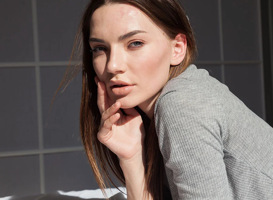 A woman with brown hair gently resting her face on her hand, gazing directly at the camera with a thoughtful expression, wearing a light grey top - Silhouette Thread Lifting in Frisco, TX